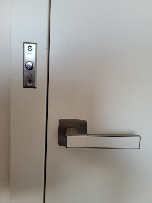 Nerezové odchodové tlačítko pro otevření elektromagnetu, čistě zadlabané do stěny vedle dveří.