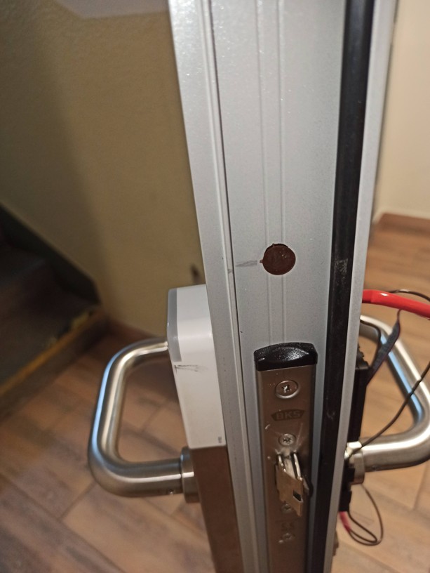 Detail hrany hliníkových dveří s nově osazeným mechanickým samozamykacím zámkem BKS a vnější částí kování Salto.