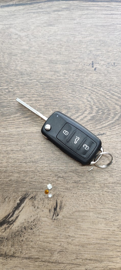Kompletně opravený a sestavený autoklíč pro VW Tiguan v novém obalu vedle poškozeného starého mikrospínače.