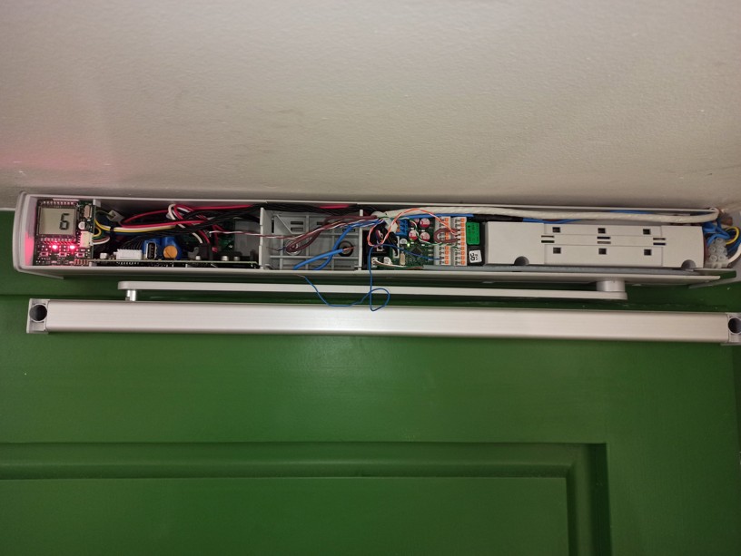 Detailní záběr na rameno automatického dveřního pohonu osazeného na protipožárních dveřích.