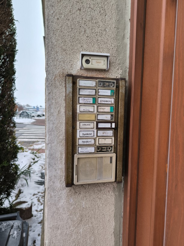 Původní zastaralé a zažloutlé zvonkové tablo u vstupu do bytového domu před plánovanou modernizací