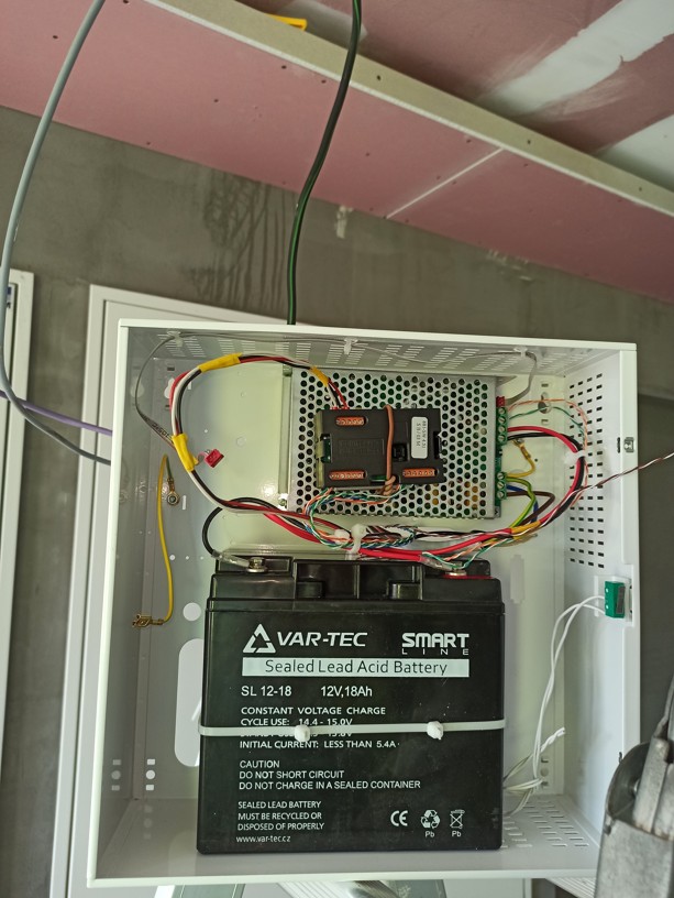 Detail otevřeného kovového boxu se záložním zdrojem a baterií pro napájení motorových zámků.