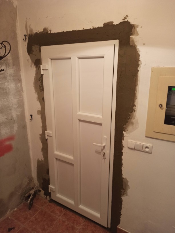 Detail zednického zapravování a začišťování ostění kolem nových dveří do hladkého finálního štuku.