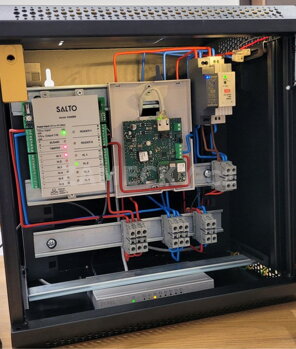 Otevřený instalační rozvaděč s profesionálně zapojenou řídící jednotkou přístupového systému Salto a síťovými prvky pro chytré otevírání dveří.