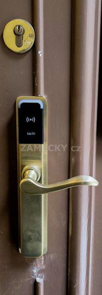Mosazné elektronické kování Salto s RFID čtečkou nainstalované na historických dřevěných dveřích v muzeu nacházejícím se v památkové zóně. Bezdrátový přístupový systém na RFID čip nebo mobil umožňuje moderní zabezpečení bez nutnosti tahání kabelů a naruše
