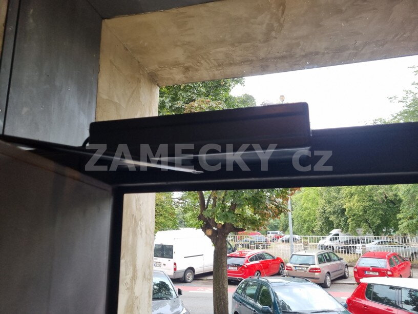 Detail instalace dveřního pohonu nastříkaného do antracitové barvy na hliníkové vstupní dveře.