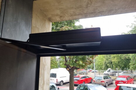 Detail instalace dveřního pohonu nastříkaného do antracitové barvy na hliníkové vstupní dveře.